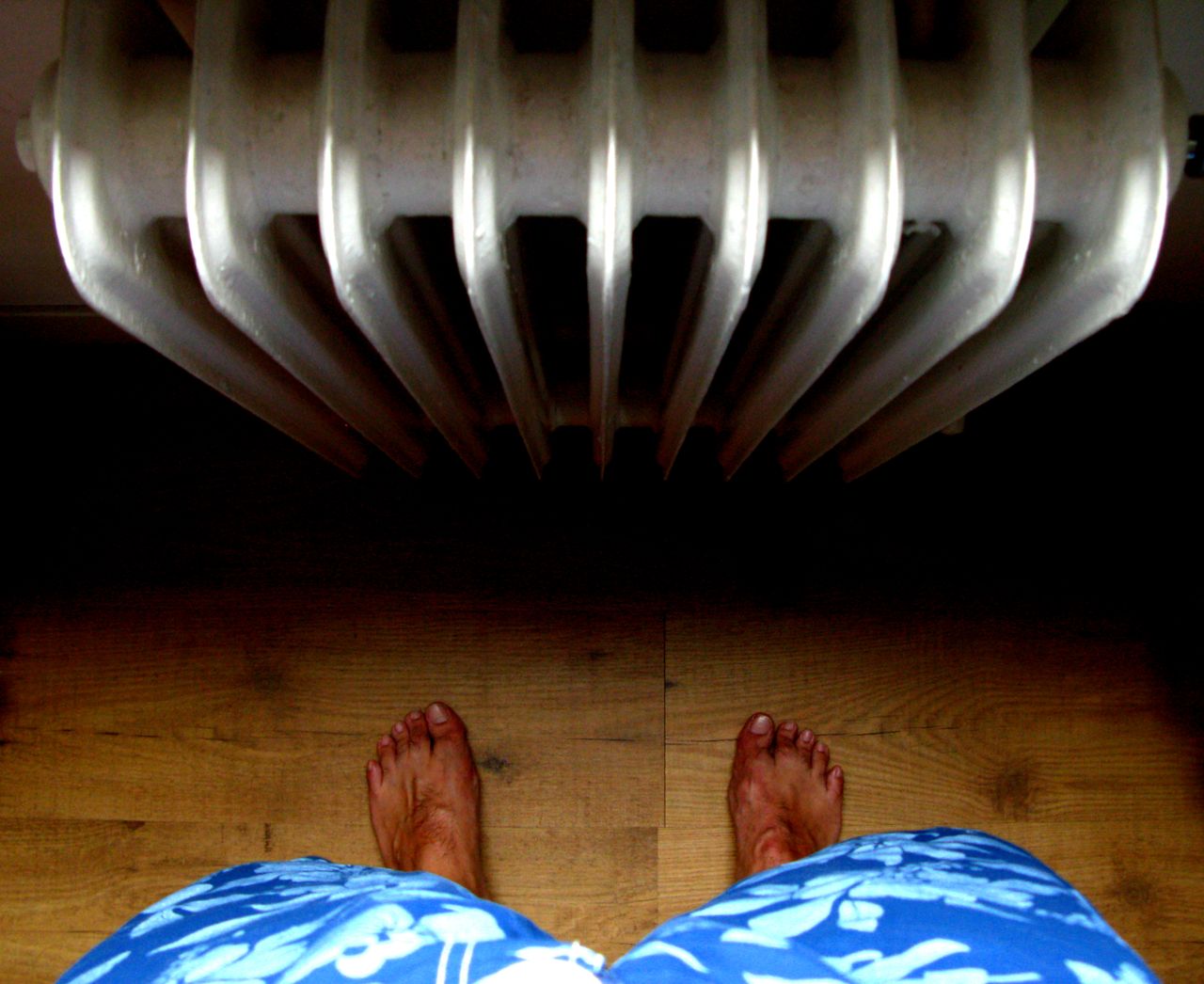 A unique perspective from above showing bare feet standing on wooden floor near a radiator.